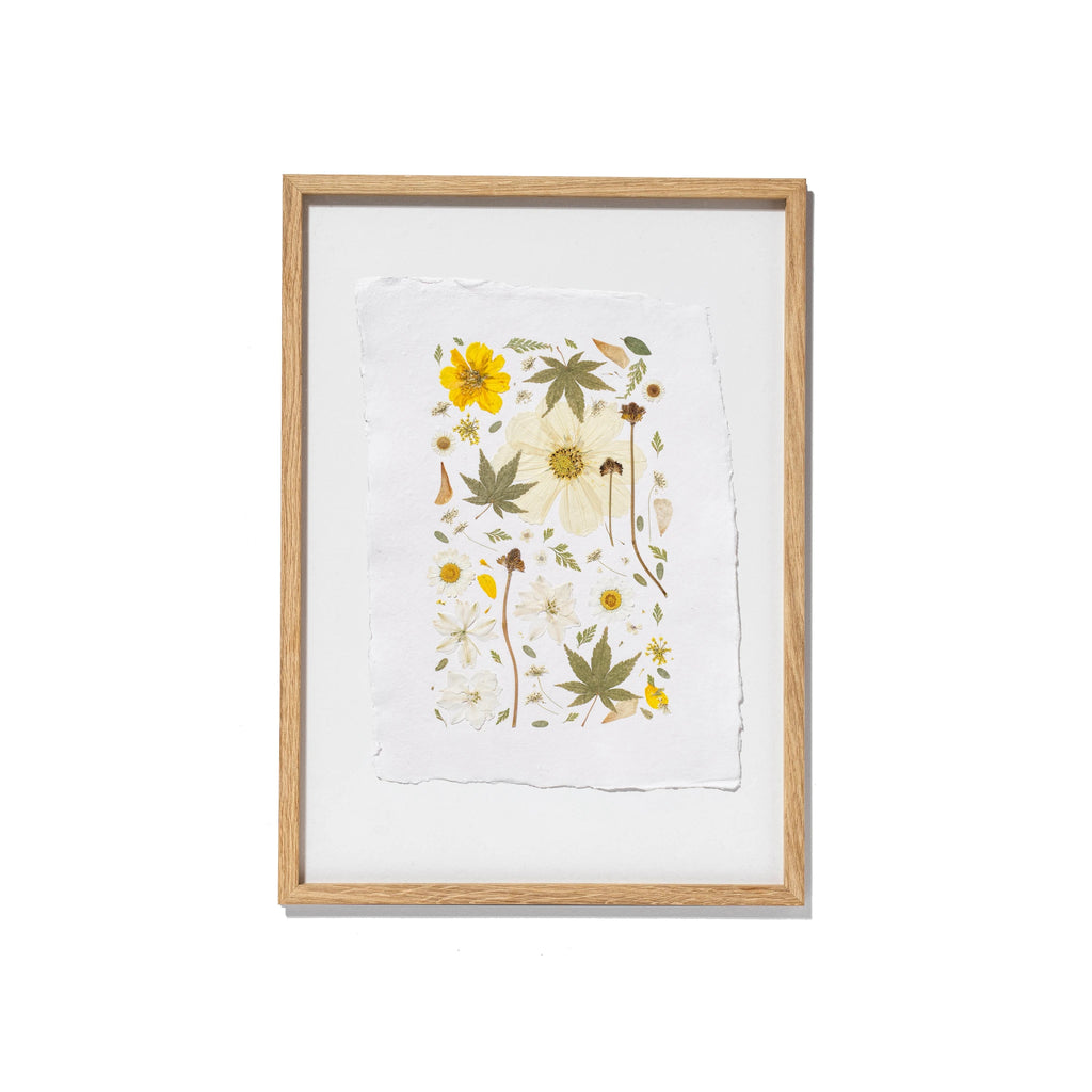 Framed botanical art print featuring pressed flowers and leaves on textured white paper, set in an oak wood frame against a white background.