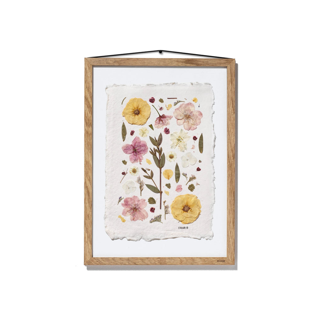 Framed botanical art featuring pressed flowers and leaves on textured off-white paper, housed in a natural oak wood frame with a black hanging string, shown against a plain white background.