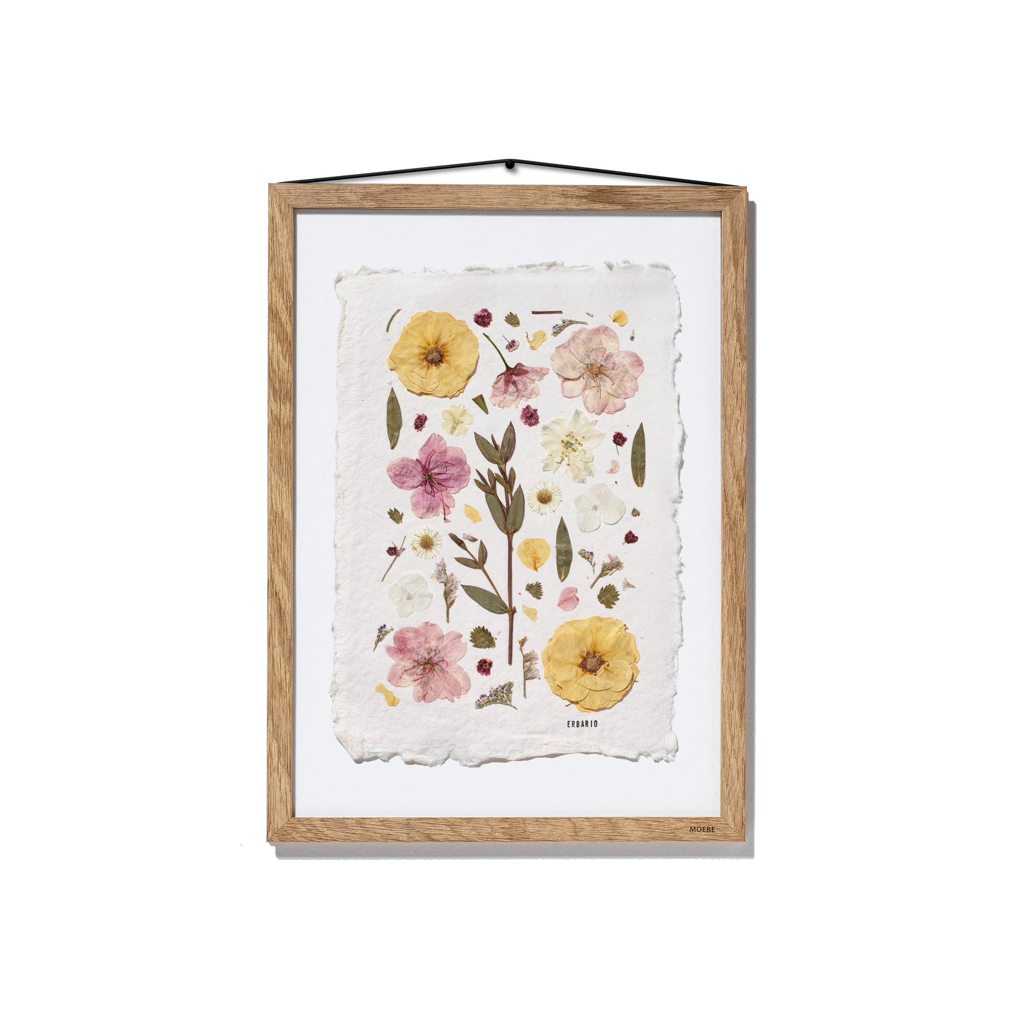 Framed botanical art featuring pressed flowers and leaves on textured off-white paper, housed in a natural oak wood frame with a black hanging string, shown against a plain white background.