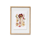 Framed botanical art featuring pressed flowers and leaves on textured white paper, set in a light natural wood frame against a white background.