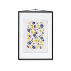 A framed floral art print featuring purple, blue and yellow pressed pansies on a textured white sheet of paper in a black frame, hung on a white background.