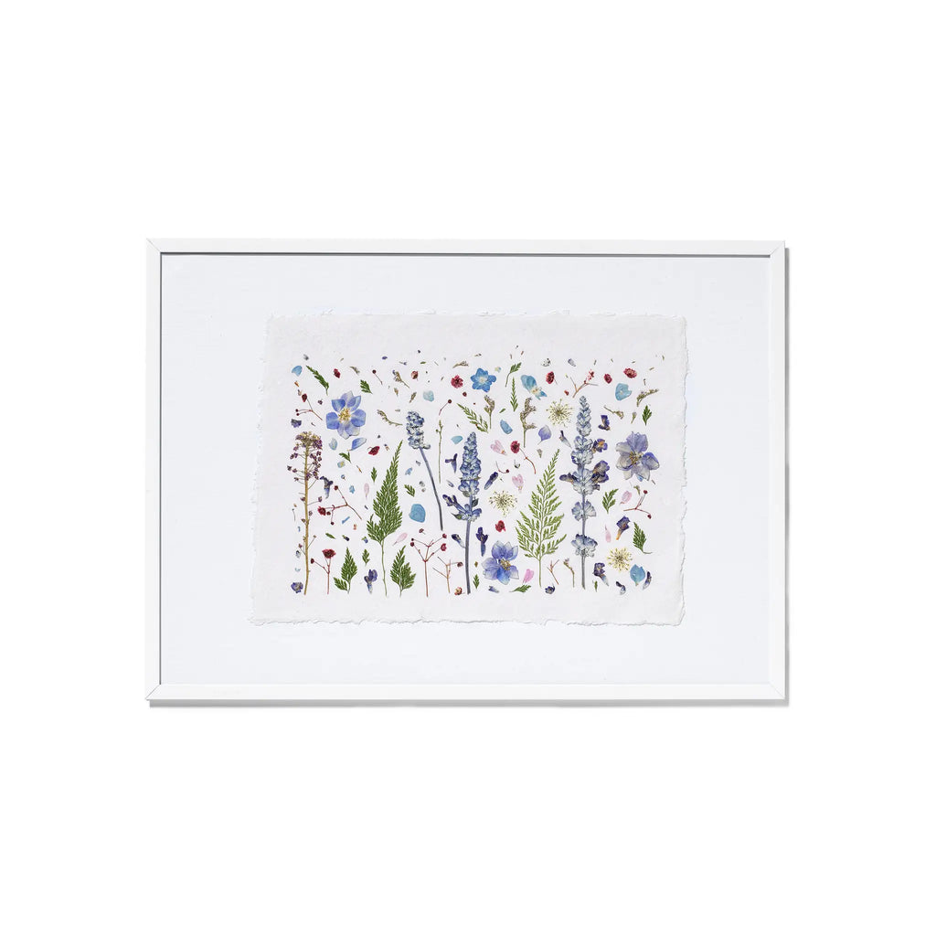 A framed botanical art featuring delicate flowers and leaves in soft blue, purple, green, and red tones on a white background, presented in a white frame against a clean white backdrop.