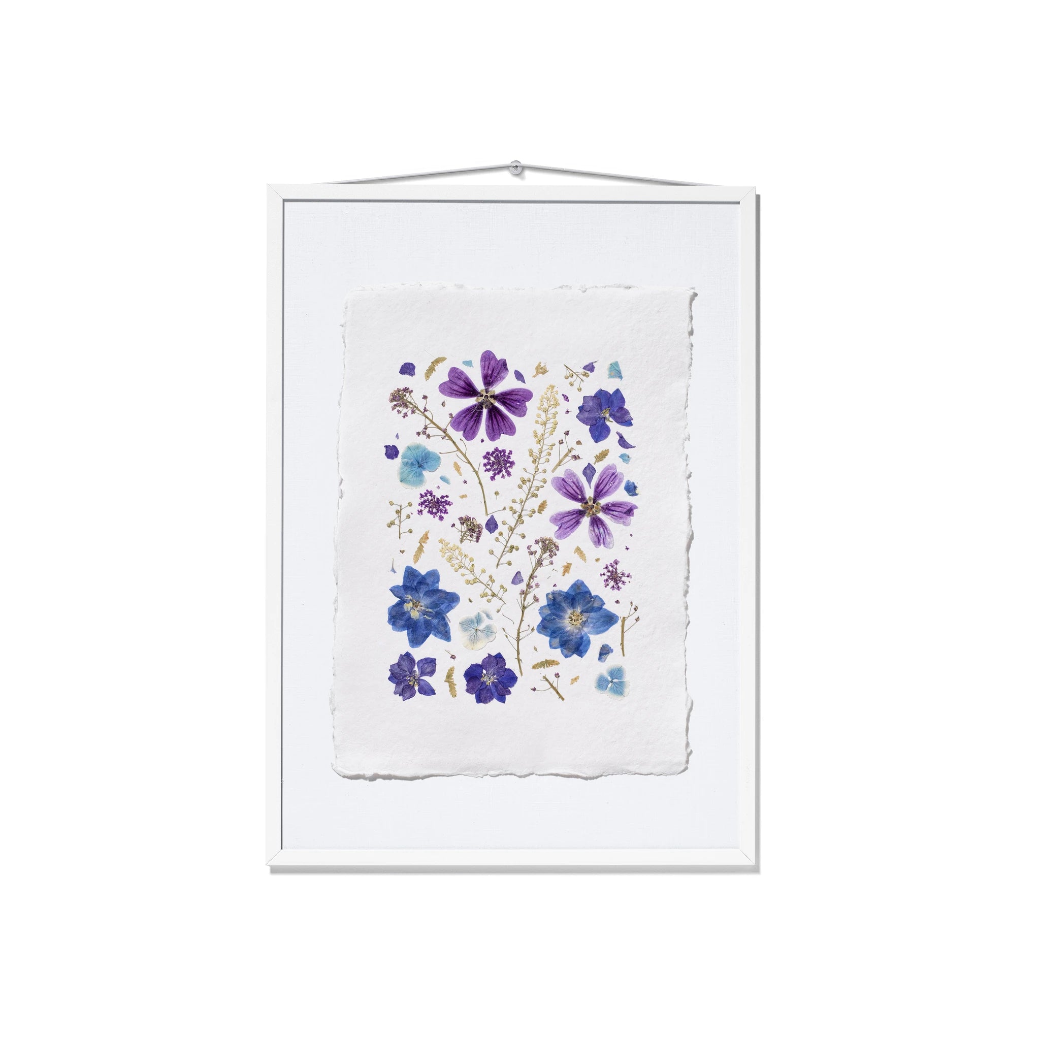 A framed botanical art print featuring pressed purple and blue flowers on a textured white paper background, housed in a white frame with a hanging wire at the top.