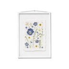 A framed botanical art featuring pressed blue and yellow flowers on a textured off-white paper background, housed in a white wooden frame with a hanging loop at the top.