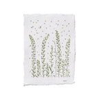A square white paper print with irregular deckled edges, featuring a botanical illustration of green wild grasses and small scattered petals, shown on a plain white background.