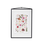 A framed botanical art featuring pressed flowers and leaves on a white textured paper background, housed in a black frame with a hanging cord.