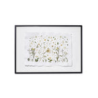 A framed botanical art featuring delicate pressed flowers and green leaves on a textured white paper background, enclosed in a black frame with a white backdrop.